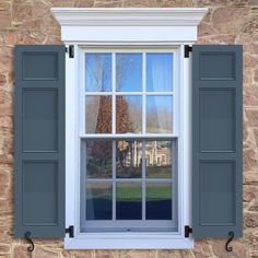 an open window with blue shutters in front of a stone wall and brick building