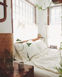 a bed with white sheets, pillows and plants in vases on the end table