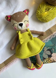 a crocheted teddy bear in a yellow dress next to some yarn and balls of yarn