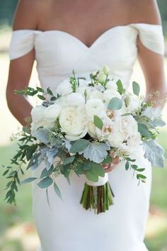 a bride holding a bouquet of white flowers and greenery