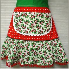 a green and red christmas apron hanging on a wall with polka dot trimmings