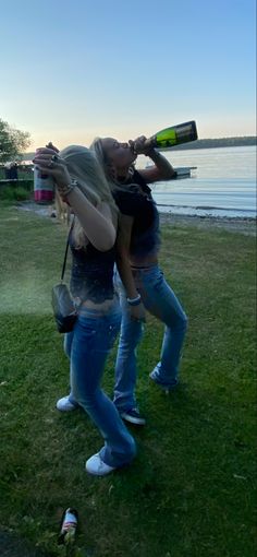 two women standing in the grass drinking from bottles