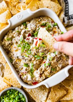 a hand dipping a tortilla chip into a bowl of dip surrounded by chips