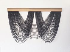 black string art hanging on the wall above a wooden shelf in a white walled room