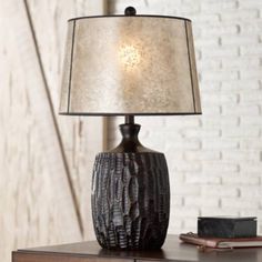 a table lamp sitting on top of a wooden desk next to a book and a brick wall