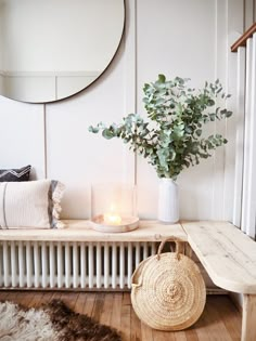 a table with a basket and candle on it next to a wall mounted round mirror