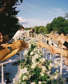 a group of people toasting wine glasses over a table with white flowers and greenery