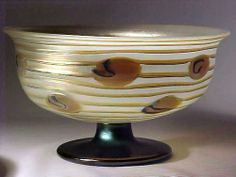 a white bowl sitting on top of a metal stand with brown designs in it's center