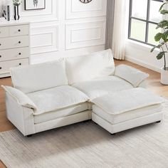 a white sectional couch in a living room with a clock on the wall behind it