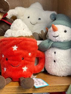 several stuffed animals are sitting on a shelf with one holding a coffee mug and the other wearing a scarf