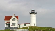 a lighthouse on top of a grassy hill next to a white house with red roof