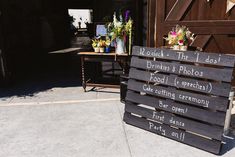 a wooden sign sitting on the side of a road next to a table with flowers