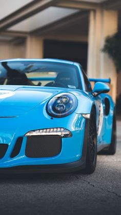 a blue porsche sports car parked in front of a building with its hood up and lights on