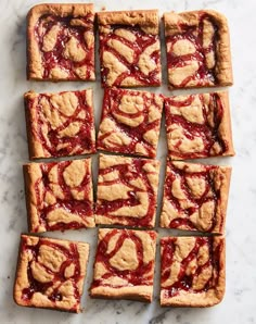 several square pieces of pie sitting on top of a white marble counter with red sauce drizzled all over them