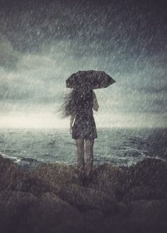 a woman holding an umbrella while standing on top of a rock next to the ocean