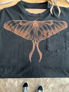 a person standing next to a black shirt with a butterfly on it's chest