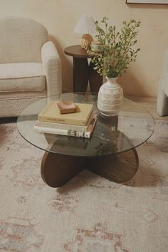 a glass table topped with books and a vase filled with flowers next to a couch