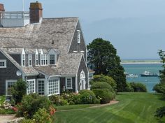 a large house sitting on top of a lush green field next to the ocean with boats in the water