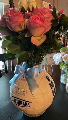 a vase filled with pink roses on top of a table next to a volleyball ball