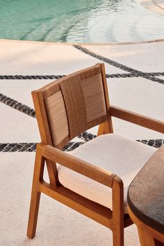 a wooden chair sitting next to a pool with a cushion on it's back