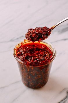 a spoon full of chili sauce on top of a white marble counter with red pepper flakes