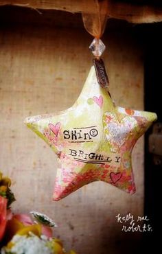 a star shaped ornament hanging from a wooden shelf with flowers in the background