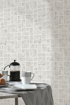 a table topped with a coffee cup and plate next to a wall covered in white tiles