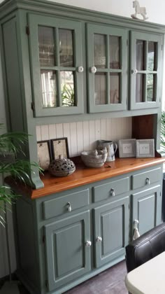 a green china cabinet with glass doors and wooden counter top in a dining room area