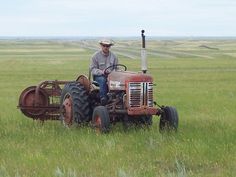 a man is sitting on an old tractor in the middle of a field with grass