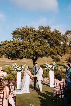 a bride and groom standing at the end of their wedding ceremony under a large tree