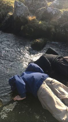 a man laying on top of a rock next to a river