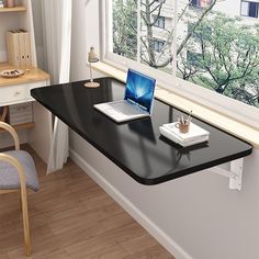 a laptop computer sitting on top of a black desk next to a window sill