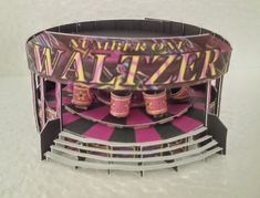 a pink and black carnival stage with three cups on it's sides that read number one walter