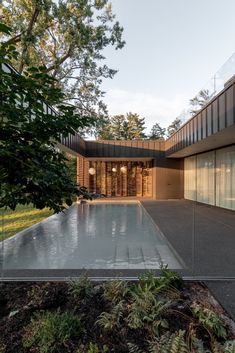 an empty swimming pool in front of a building with glass walls and trees around it