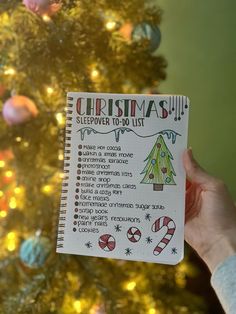 someone holding up a christmas list in front of a christmas tree