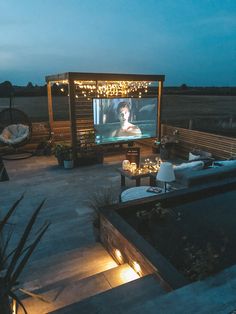 an outdoor movie screen is lit up at night with lights on the patio and furniture