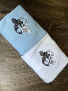 two folded towels with cats and bats on them sitting on a wooden floor next to each other