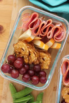 two plastic containers filled with food sitting on top of a wooden table next to grapes