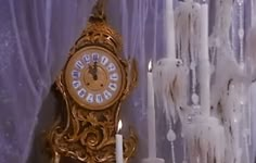 a gold clock sitting on top of a table next to a white candle and curtain