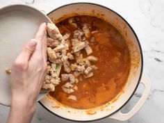 a person is adding meat to a stew in a large pot on the counter top