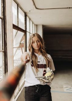 a young woman holding a baseball bat in her right hand and pointing at the camera