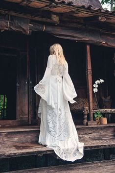 a woman in a long white dress standing on a porch with her back to the camera