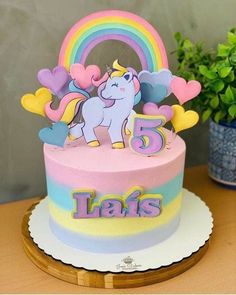 a birthday cake with a unicorn on top and rainbow decorations in the middle, sitting on a table next to a potted plant