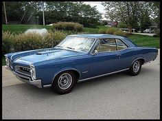 an old blue car is parked on the side of the road in front of some bushes