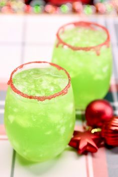 two glasses filled with green liquid sitting on top of a checkered table cloth next to christmas decorations