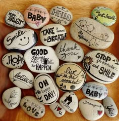 some rocks with writing on them are arranged in a wooden bowl, and one has a baby's name written on it