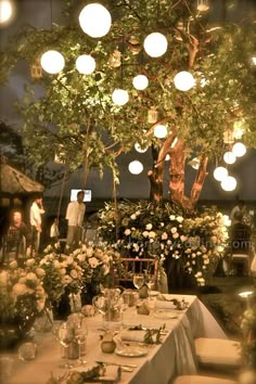 a dining table set up under a tree with lights hanging from it's branches