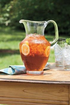 a pitcher and three glasses on a wooden table with green grass in the back ground