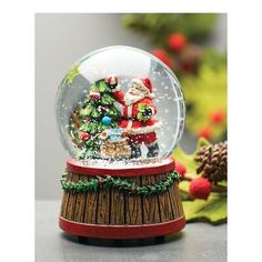 a snow globe with santa clause and christmas tree inside it on a table next to pine cones