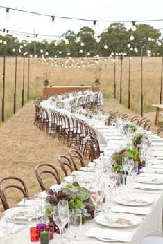 a long table is set up with place settings for an outdoor dinner party in the middle of a field